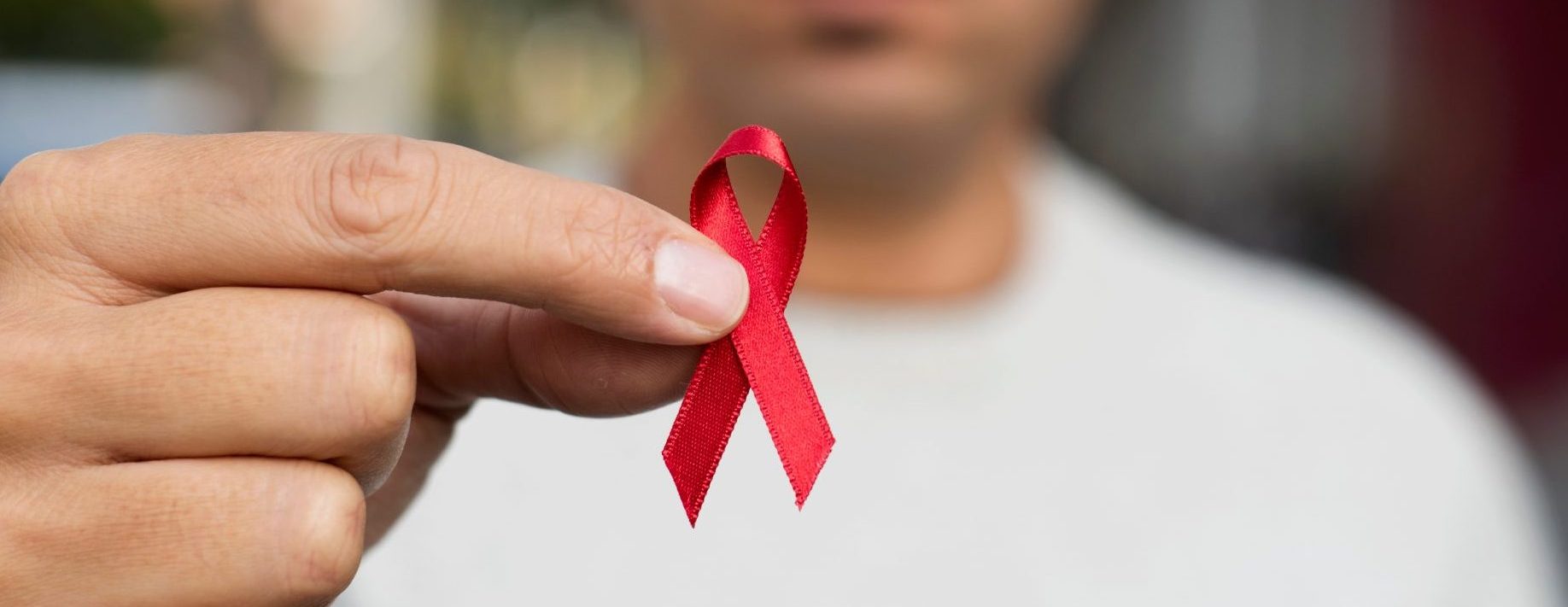 closeup of a young man with a red awareness ribbon for the fight against AIDS in his hand